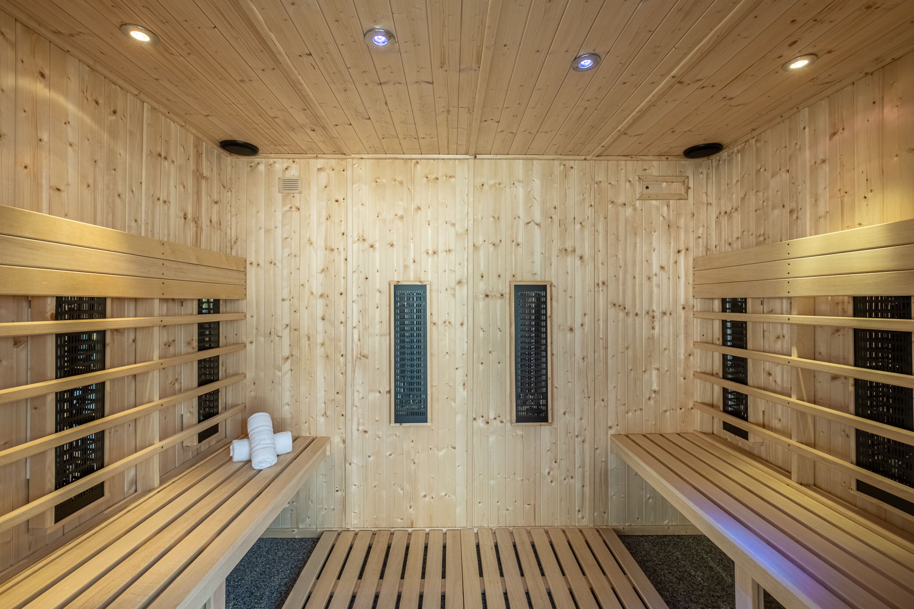 Una sala de sauna con bancos y asientos de madera, suelo de madera e iluminación empotrada en el techo.