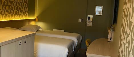 Une chambre d’hôtel avec deux lits, un bureau en bois, une petite télévision et un mur décoré d’un motif.