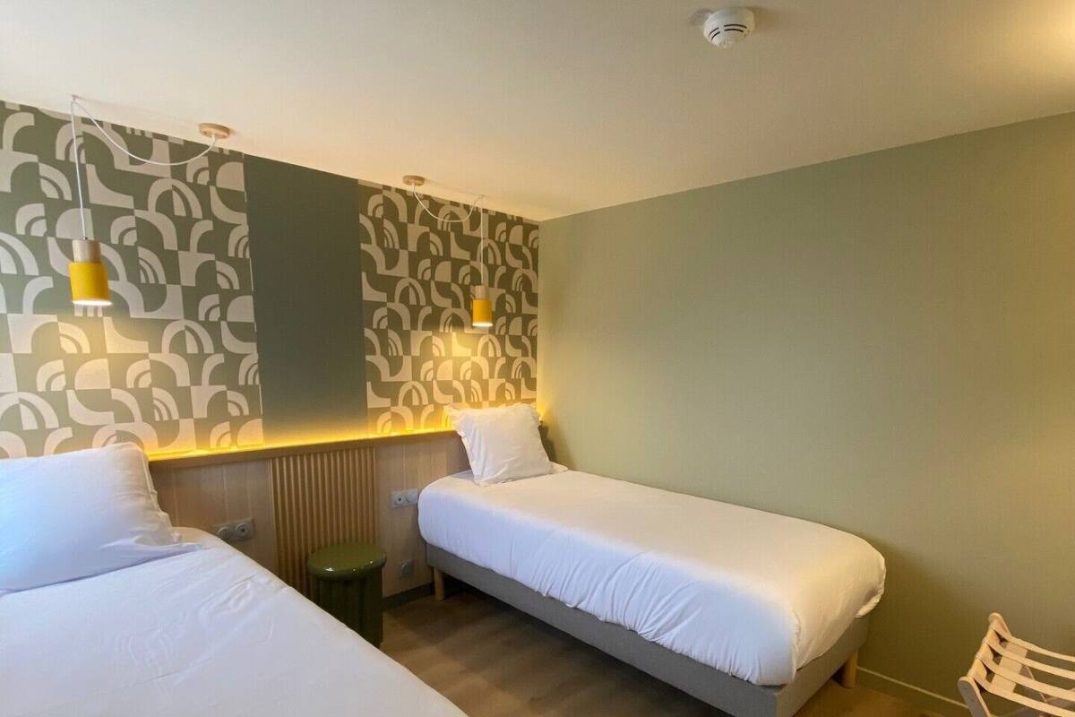 Ein Hotelzimmer mit zwei Einzelbetten, Holzboden, einem gemusterten Wandbild und einem Stuhl.