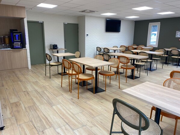 Une pièce spacieuse avec plusieurs tables et chaises, un distributeur automatique et un téléviseur fixé au mur.