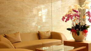 Una sala moderna con un sofá color beige, una mesa de centro de vidrio y un jarrón con orquídeas.