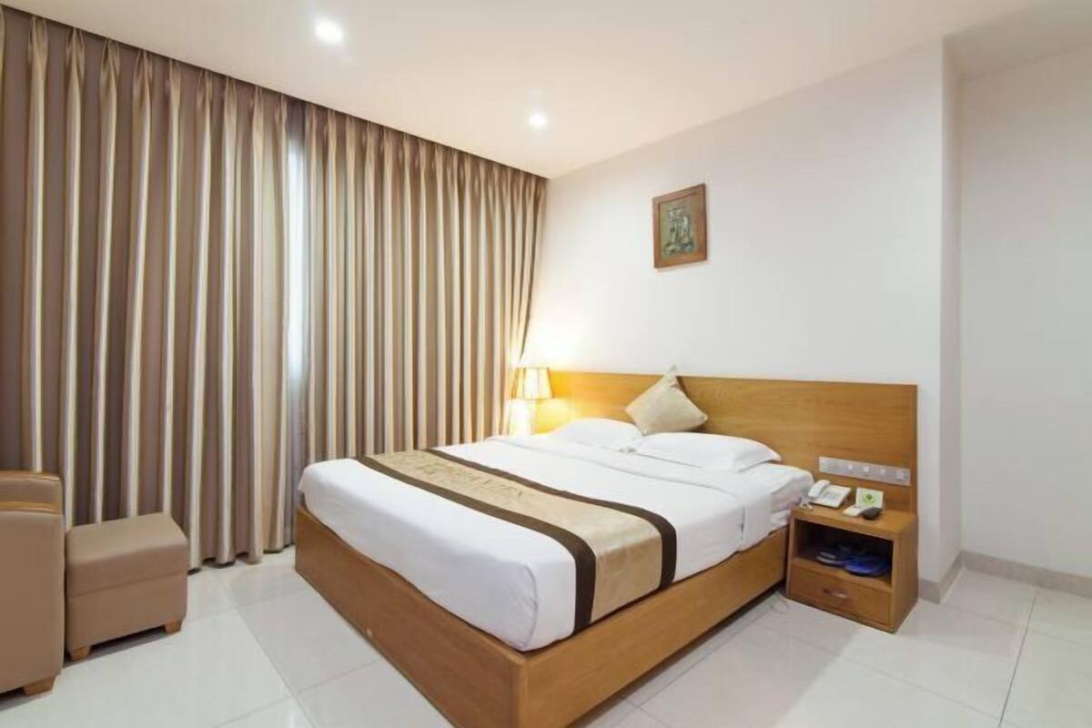 A hotel room with a bed, bedside table, lamp, and curtains.