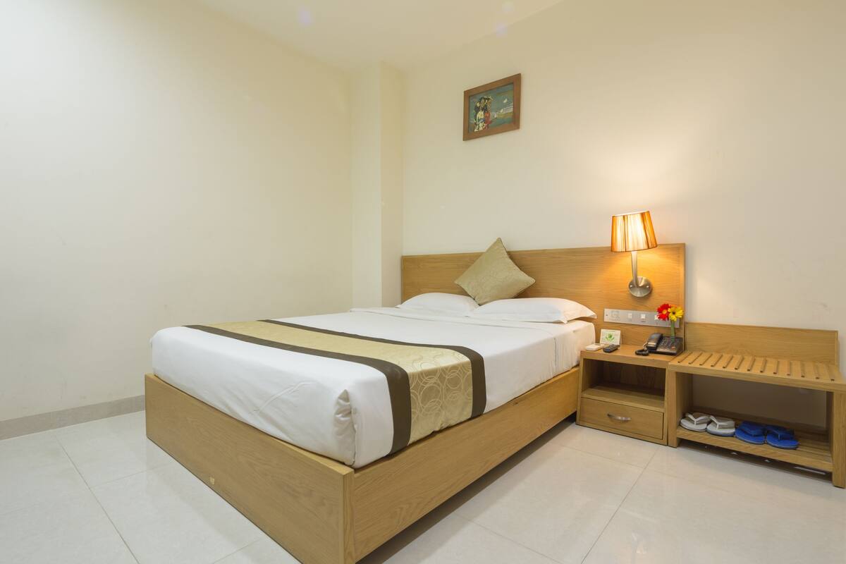 A neatly arranged hotel room with a wooden bed, a bedside table with a lamp, and a shelf with shoes.