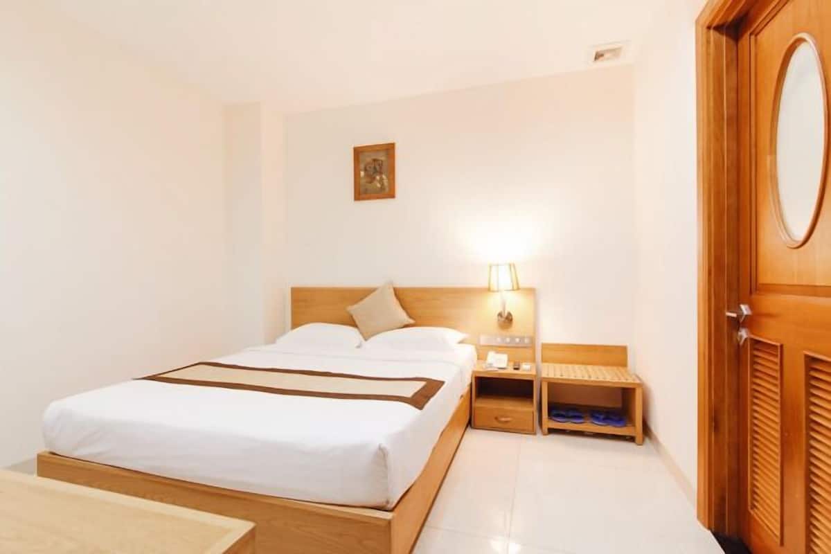 A hotel room with a bed, bedside table, lamp, and a wooden door.