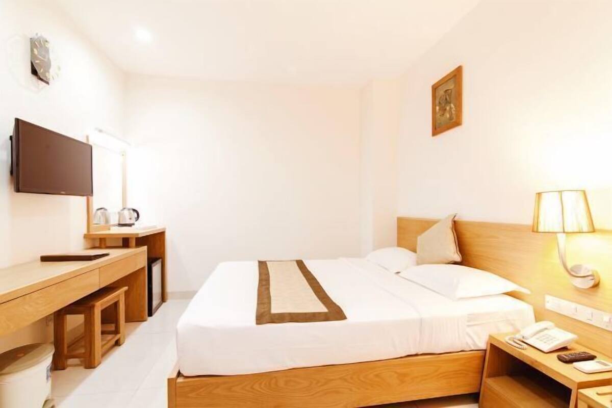 A hotel room with a bed, bedside table, desk, chair, lamp, and a flat-screen TV.