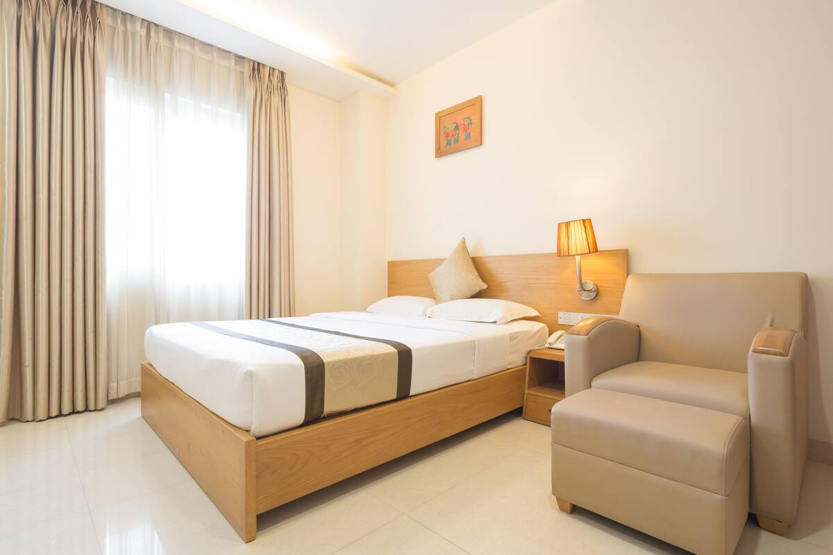 A hotel room with a wooden bed, a bedside table, a chair, and a lamp.
