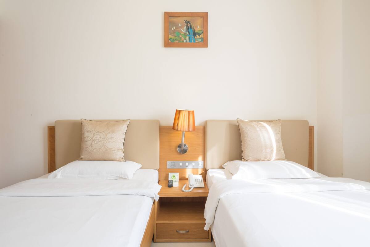 A hotel room with two beds, a nightstand with a lamp, a phone, and a painting on the wall.