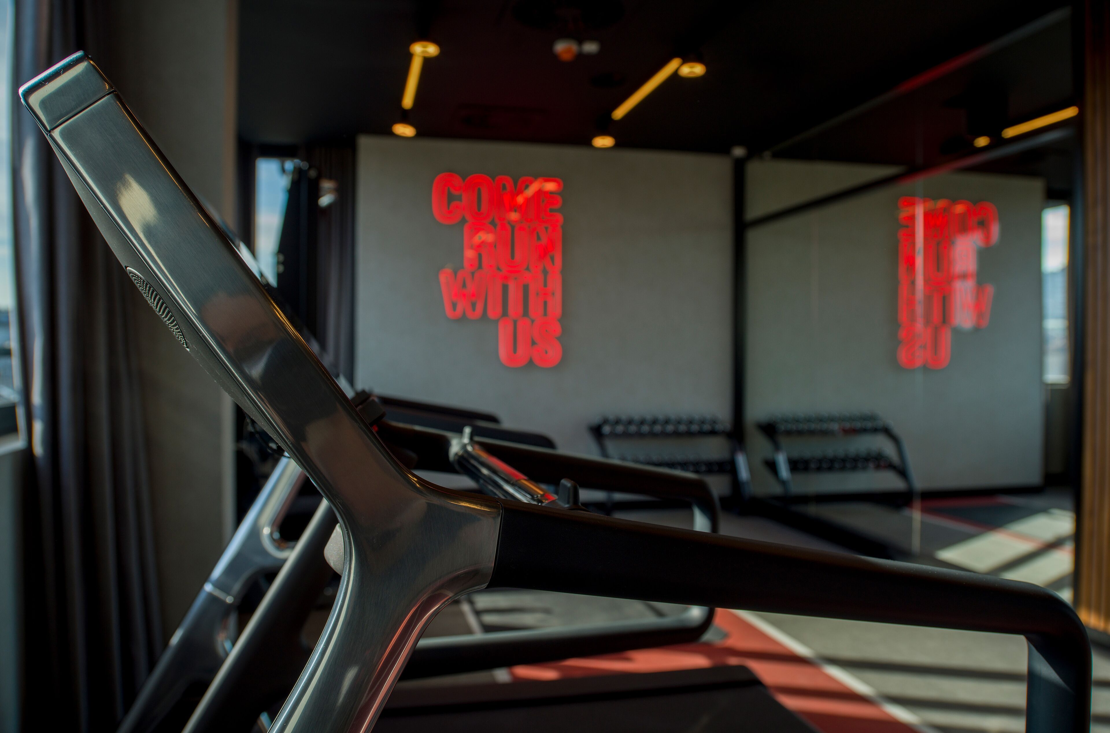 A modern interior with a prominent red sign reading "COME FROM WITH US" and a glimpse of a seating area with red and black accents.