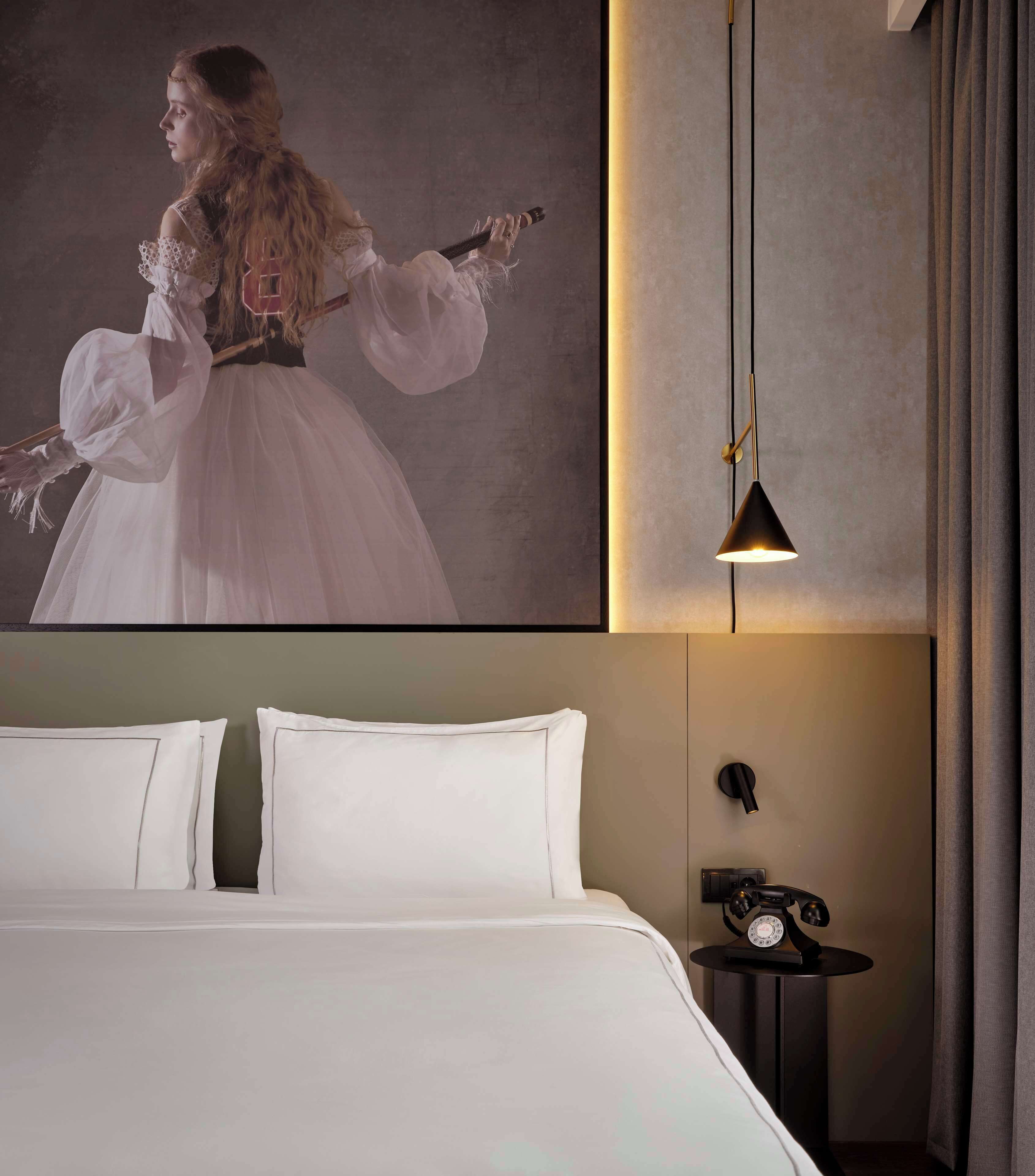 A bedroom with a bed, pillows, a nightstand with a telephone, and a wall-mounted light fixture.