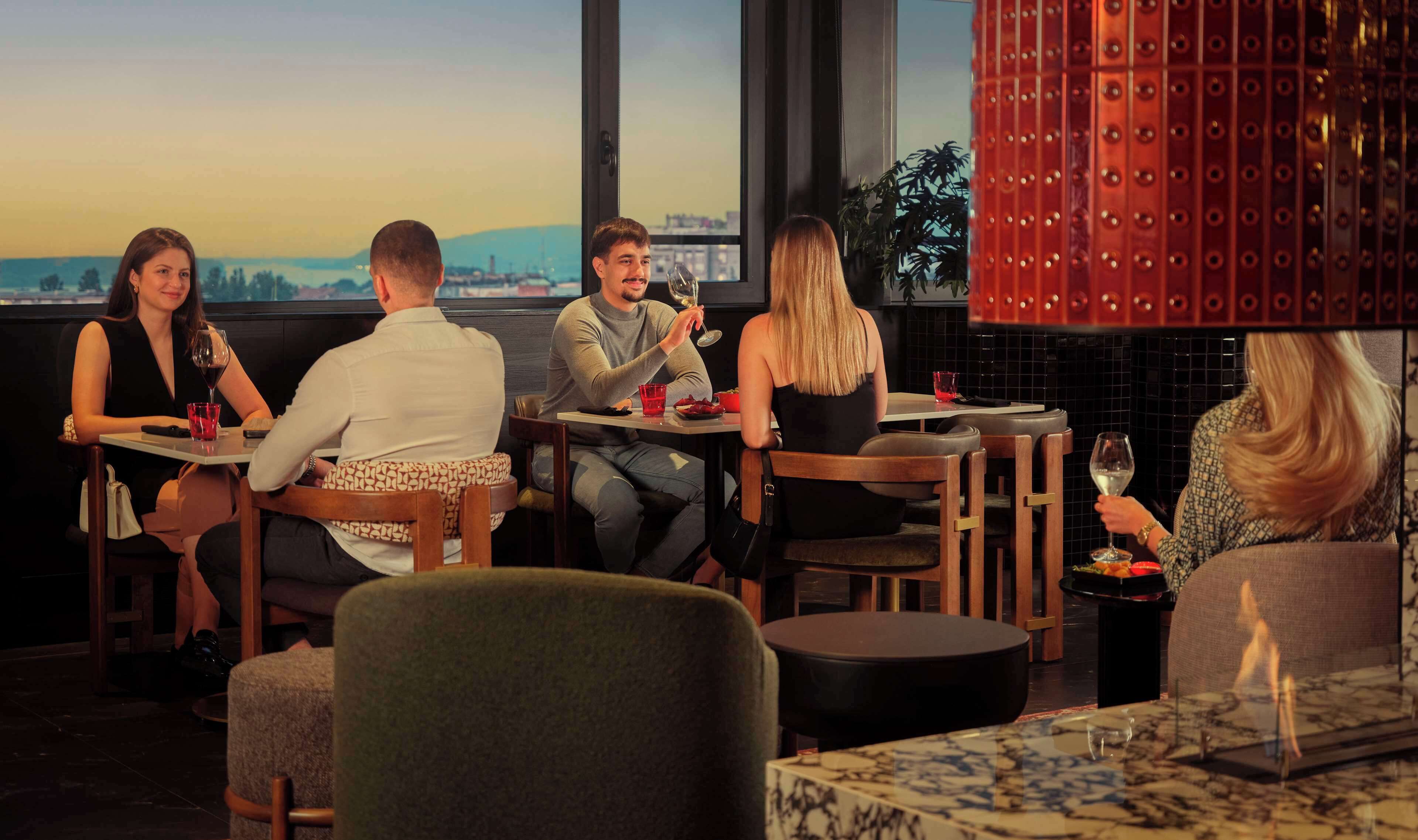 Un restaurante con vistas a la ciudad, muebles de madera y un elemento decorativo rojo.