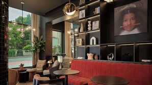 Un intérieur moderne avec un coin salon aux fauteuils recouverts de tissu rouge, une table basse et une bibliothèque agrémentée de divers objets décoratifs.