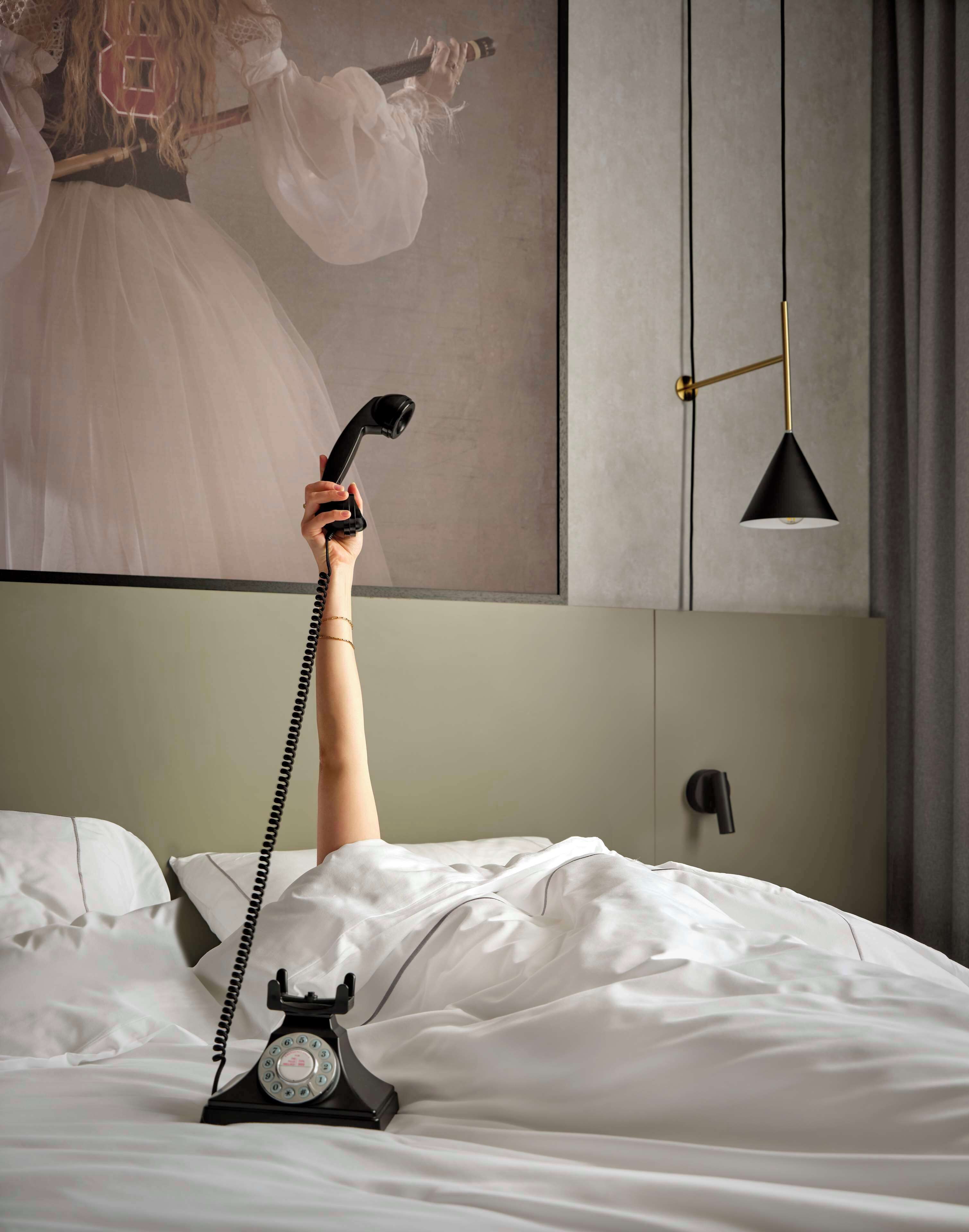 Ein Bett mit weißen Leinen, ein altes Wähltelefon und eine moderne Pendelleuchte.