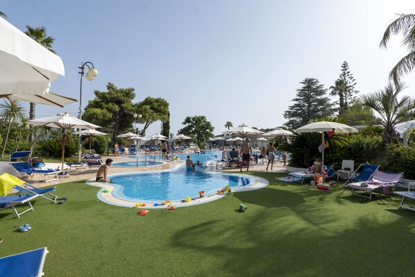 A pool area with artificial grass, lounge chairs, and umbrellas. - Hotel Santa Lucia (Santa Cesarea Terme)