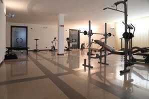 A spacious gym with various exercise equipment, a bench, and a door in the background. - Hotel Santa Lucia (Santa Cesarea Terme)