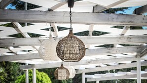 An outdoor seating area with white and orange furniture, hanging lights, and a view of greenery. - Hotel Santa Lucia (Santa Cesarea Terme)