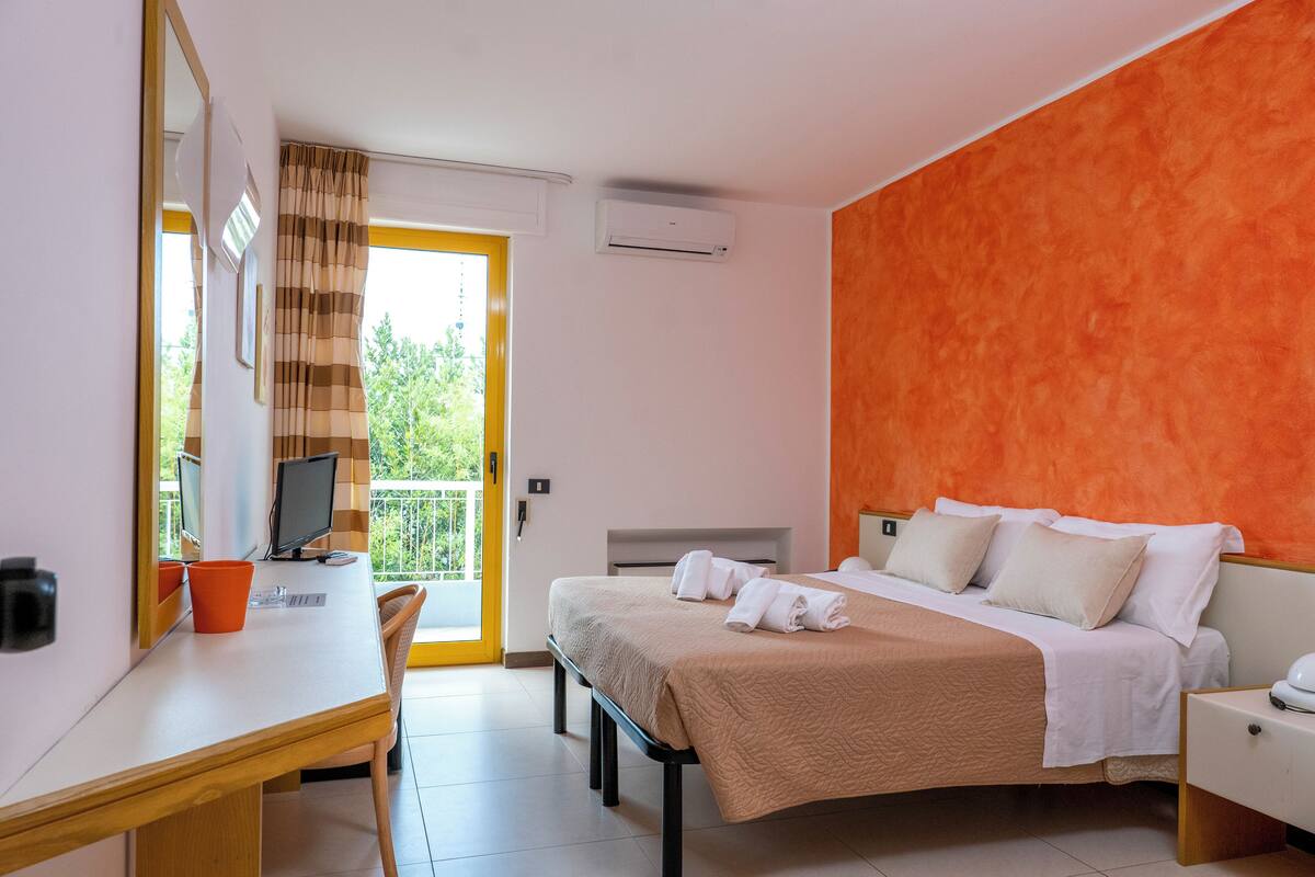 A hotel room with a bed, a desk, a chair, a TV, and a window with curtains.