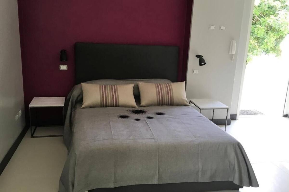 A bedroom with a bed, a nightstand, a bedside table, and a lamp.