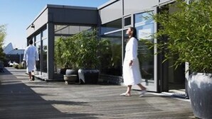 A modern building with a glass facade, a wooden deck, and potted plants. - Aspria Berlin Ku’damm – Sport & Spa (Berlin)