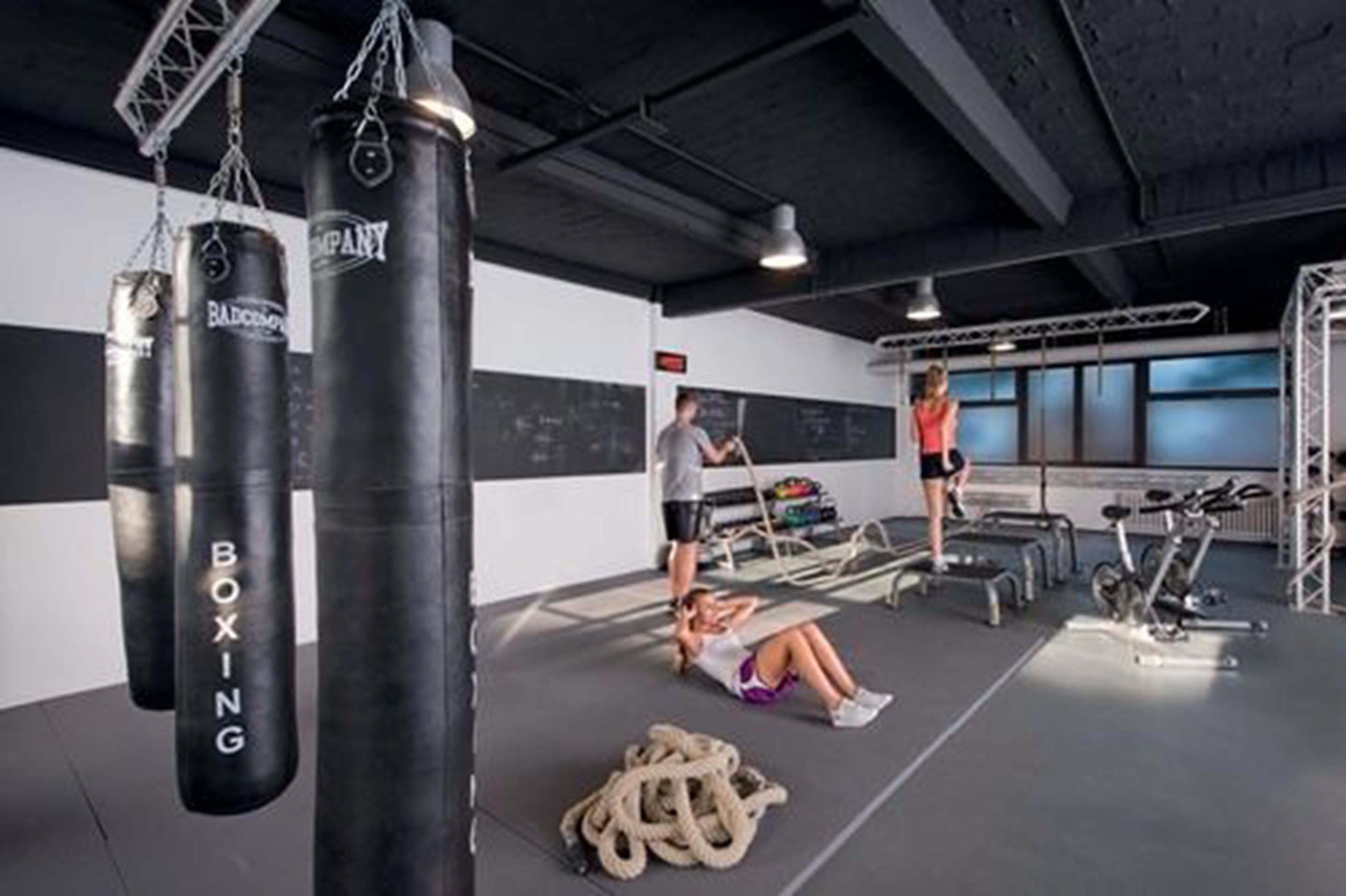 A gym with punching bags, exercise equipment, and a person doing floor exercises.
