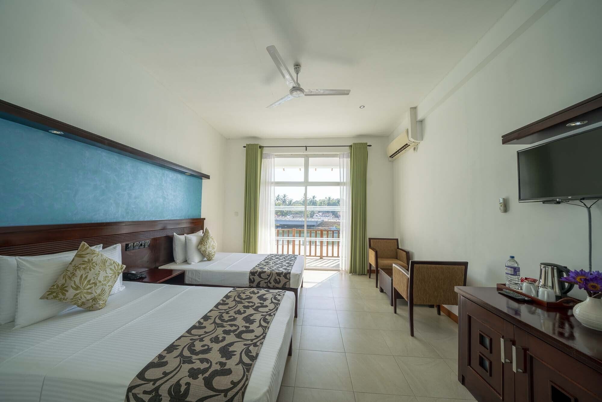 A hotel room with two beds, a ceiling fan, a TV, a desk, and a view of the outside.