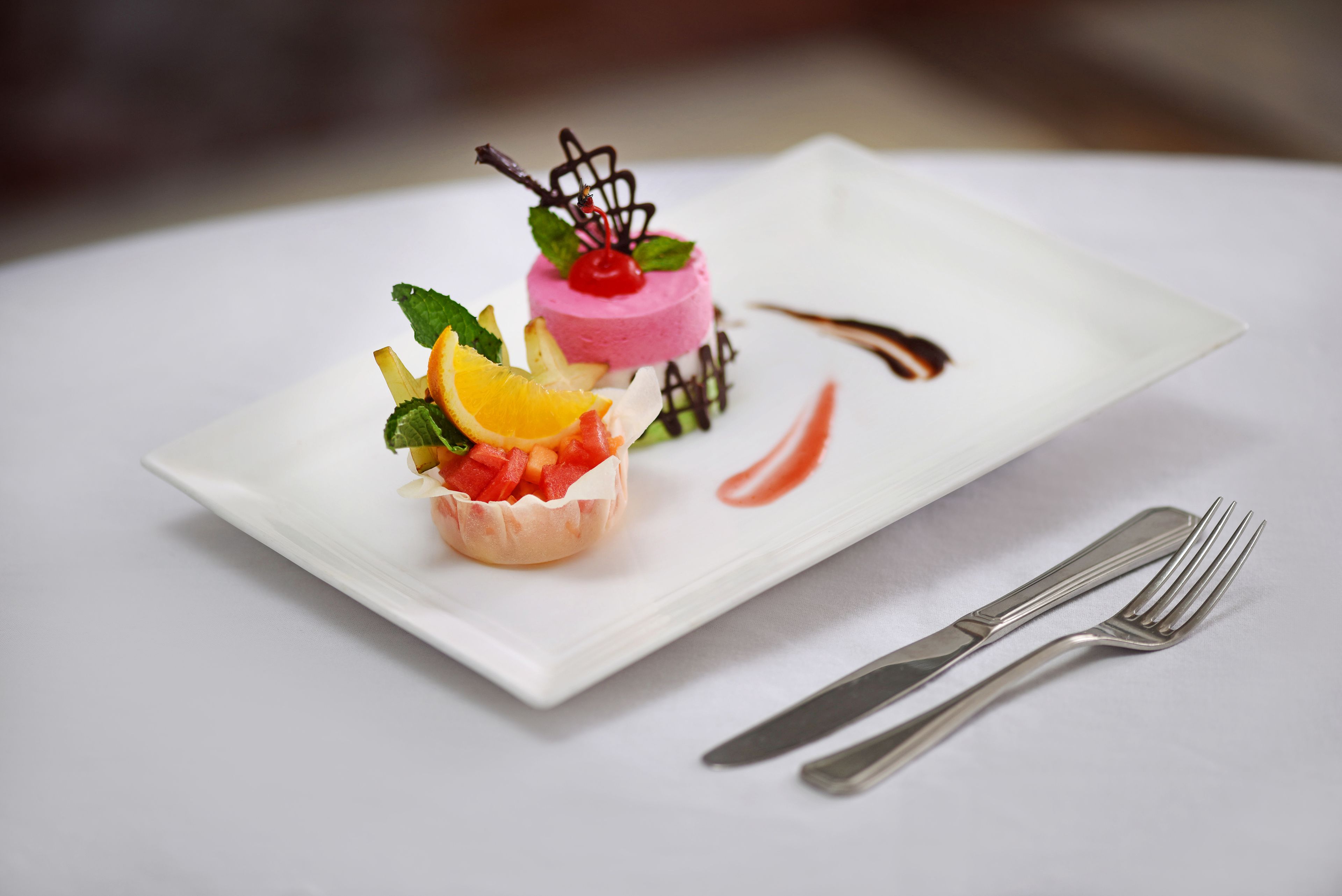 En desserttallerken med en lyserød og hvid lagkage, et fad med frugt og chokoladedrys.