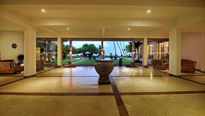 A spacious lobby with a large central planter, seating areas, and large windows offering views of the outdoors. - Mandara Resort (Weligama)
