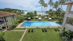A pool area with lounge chairs and umbrellas, surrounded by palm trees and a view of the ocean. - Mandara Resort (Weligama)