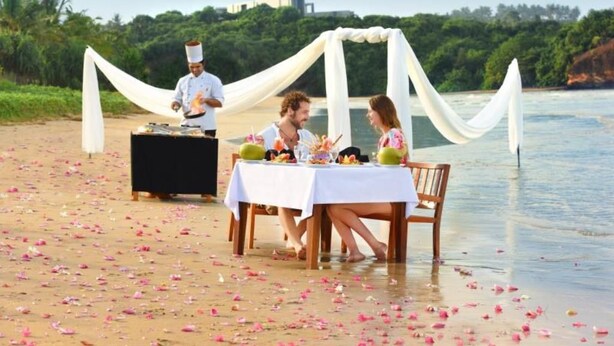 A beachside dining setup with a table and chairs, a chef, and a white draped canopy. - Mandara Resort (Weligama)