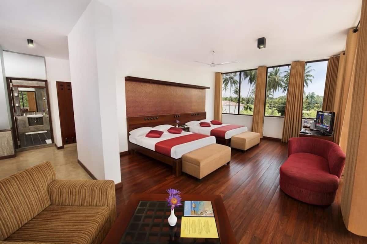 A hotel room with a large bed, two bedside tables, a red armchair, a wooden coffee table, and a TV.