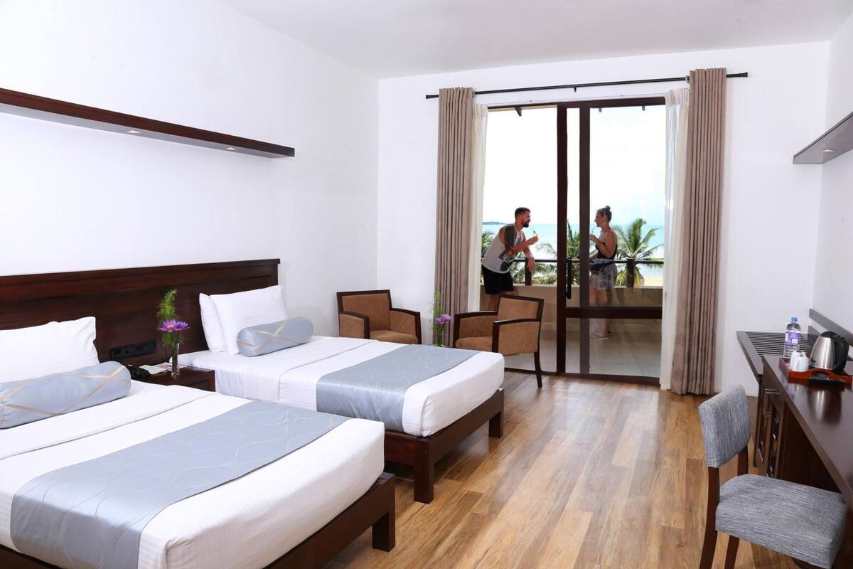 A hotel room with two beds, a desk, and a balcony with a view.