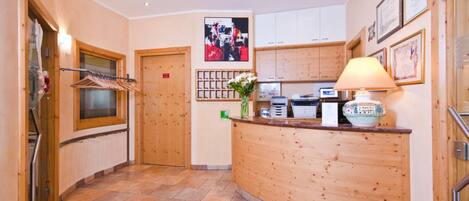 A reception area with a wooden reception desk, a wall-mounted photo, a lamp, and a small plant.