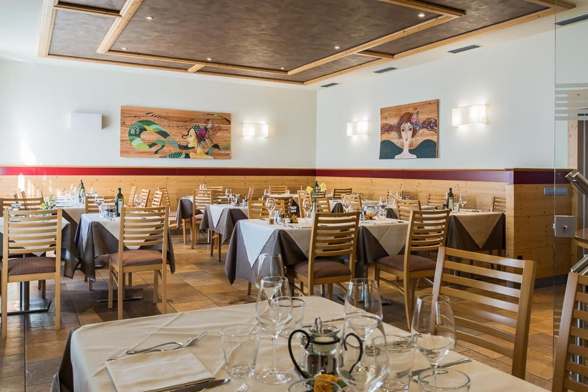 A restaurant with multiple tables set for dining, wooden chairs, and artwork on the walls.