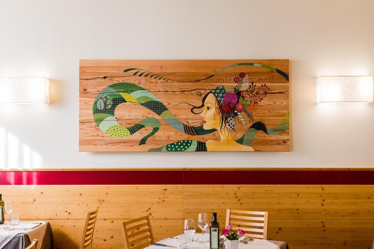 Ein Essbereich mit einer Holzwand und einem großen Gemälde über einem Tisch, gedeckt mit Weingläsern und einer Weinflasche.