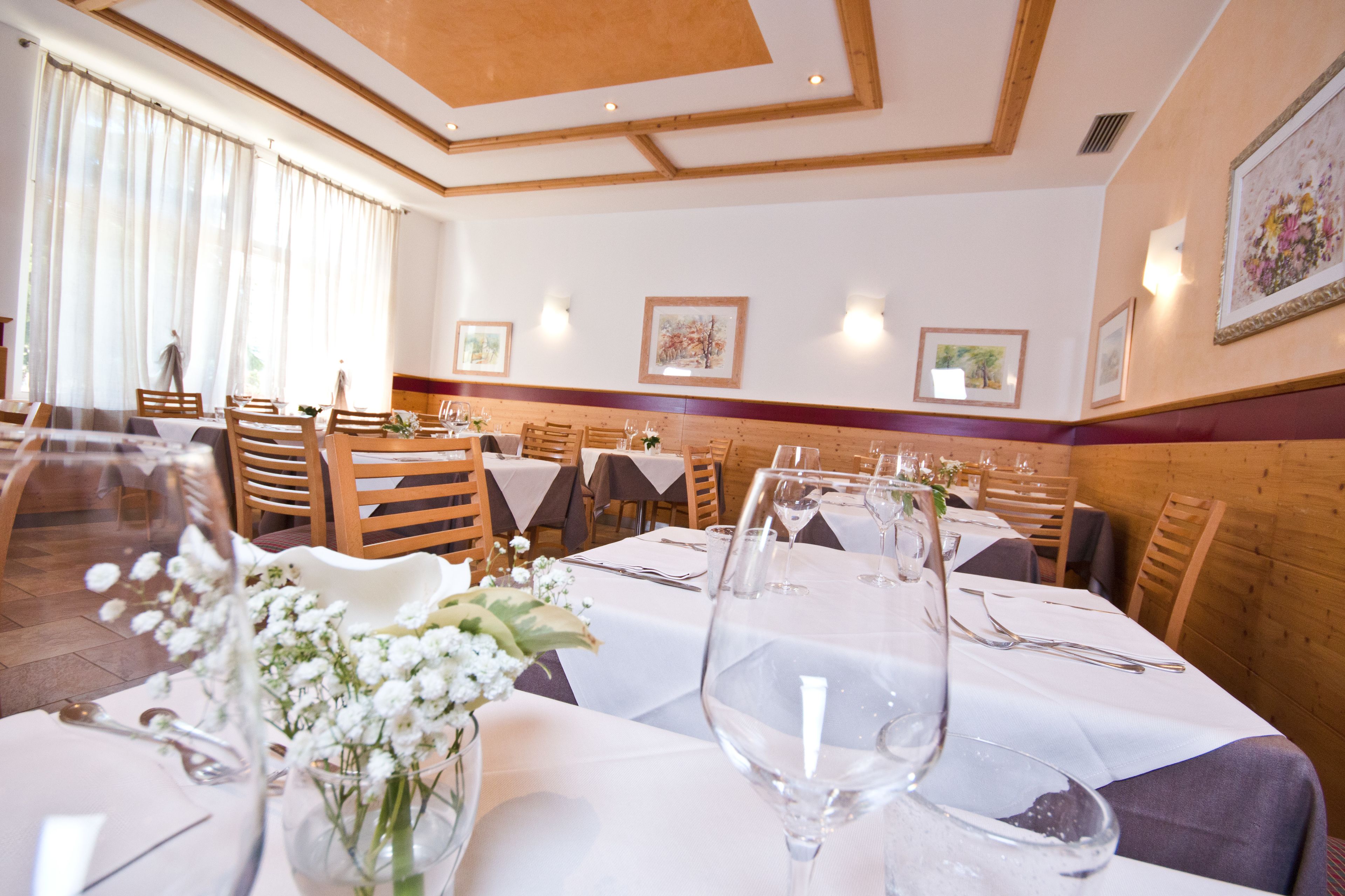 Un restaurant où les tables sont dressées pour le service, avec des nappes blanches et des centres de table floraux.