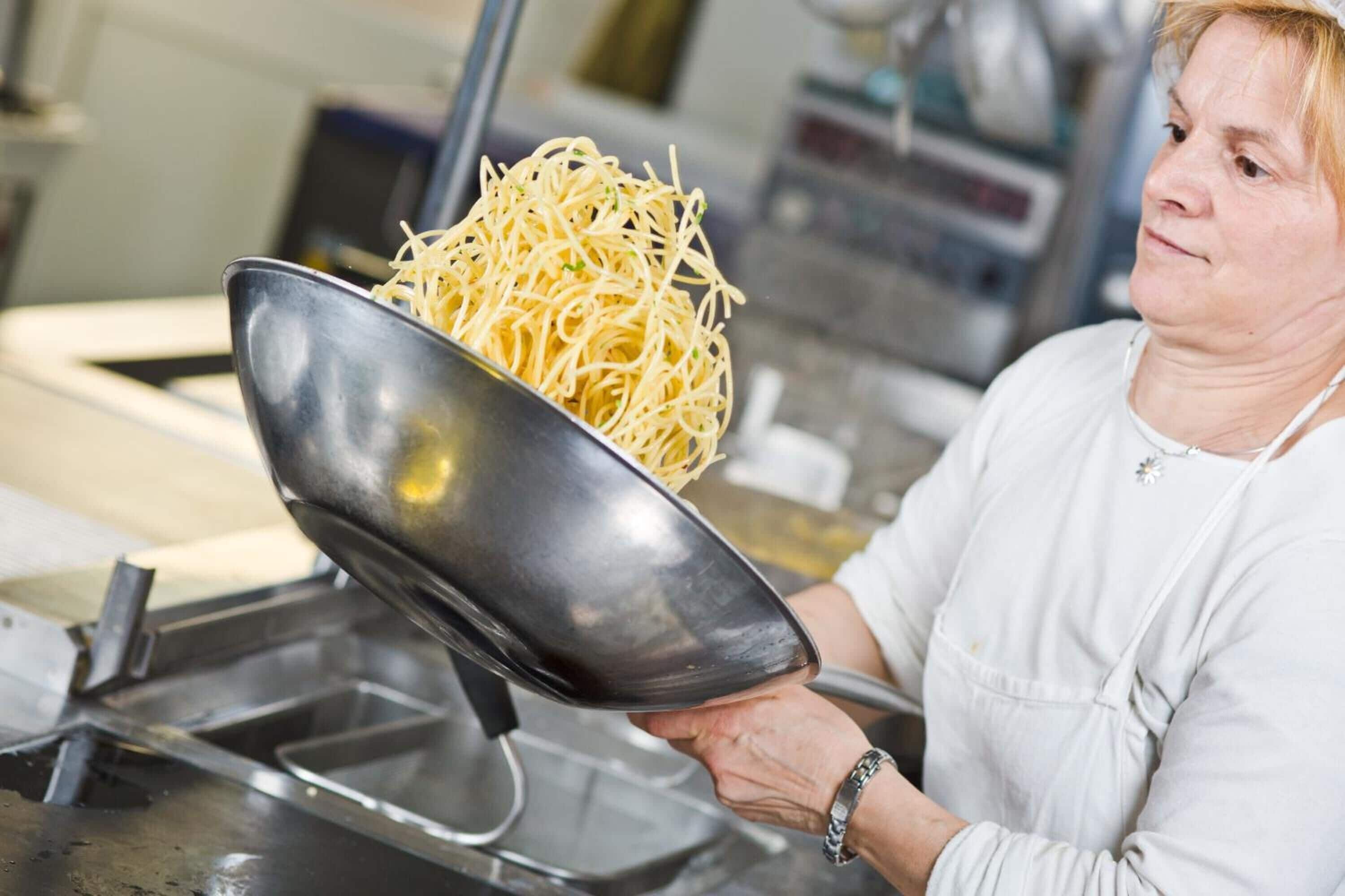 Une personne tenant un bol en métal rempli de spaghettis.