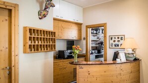 A wooden reception desk with a vase of tulips, wooden cabinets, a wall-mounted guitar, and a framed picture on the wall. - Hotel Martinelli (Ronzo-Chienis)