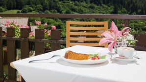 A table with a slice of cake, a plate with strawberries, and a cup of coffee on a balcony with a wooden railing and a view of a forested area. - Hotel Martinelli (Ronzo-Chienis)
