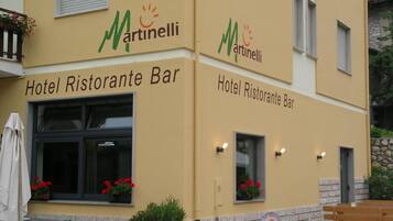Ein Gebäude mit der Beschriftung "Hotel Ristorante Bar" und dem Logo "Martinelli". Vor dem Gebäude steht ein Fahrrad, eine hölzerne Bank und Kübelpflanzen.