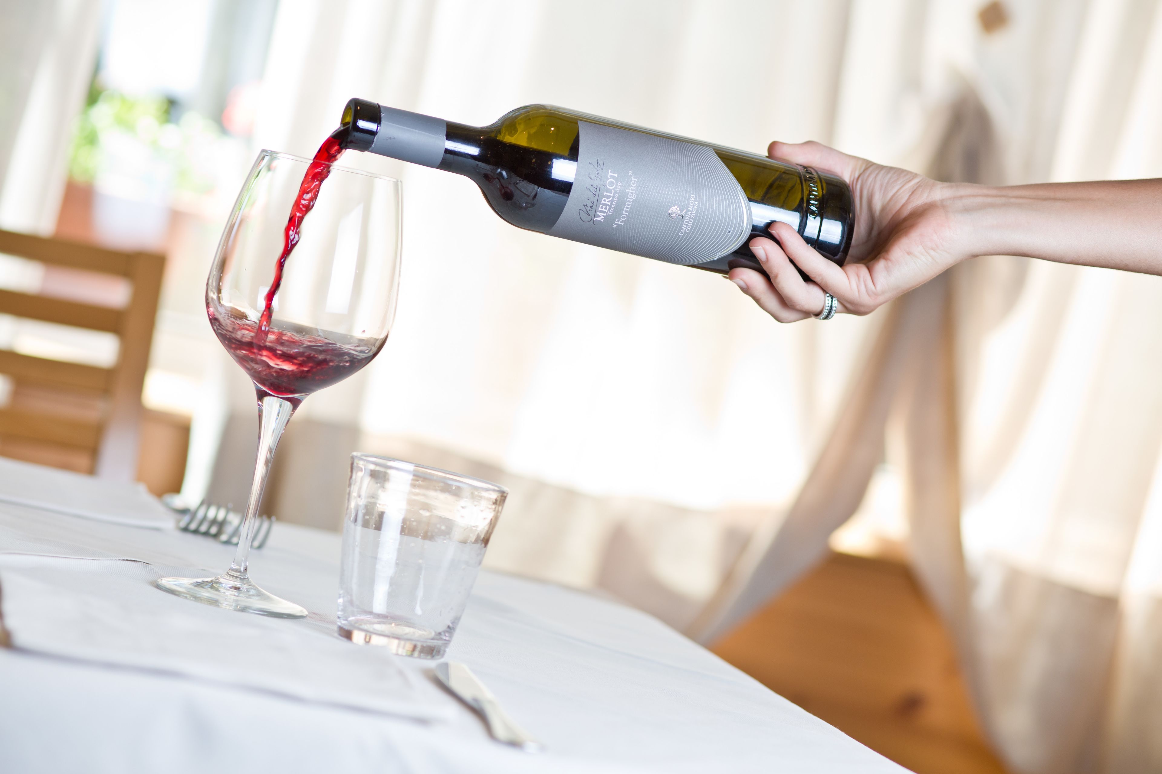 A hand pouring red wine from a bottle into a glass.