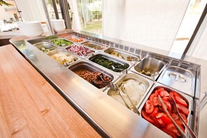 Un bufé con diversas opciones de comida, como frijoles, arroz, vegetales y tomates.