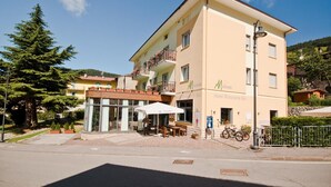 A multi-story hotel with a restaurant bar on the ground floor, outdoor seating, and a mountain backdrop. - Hotel Martinelli (Ronzo-Chienis)