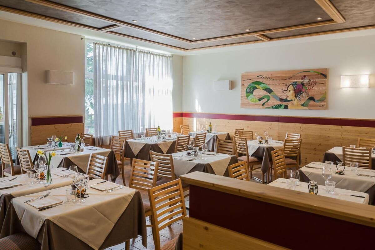 A restaurant with multiple tables set for dining, wooden chairs, and a large painting on the wall.