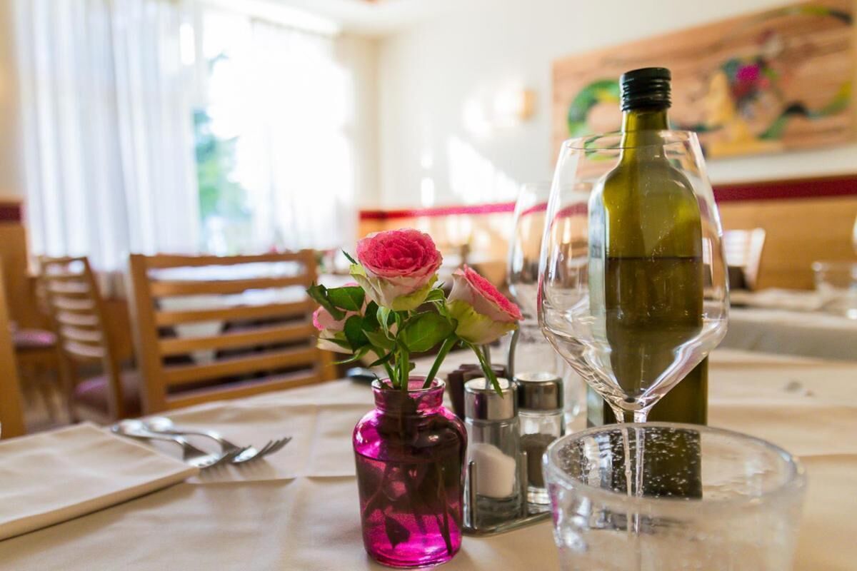 Una mesa de comedor con un jarrón rosa lleno de flores, una botella de vino y una copa.