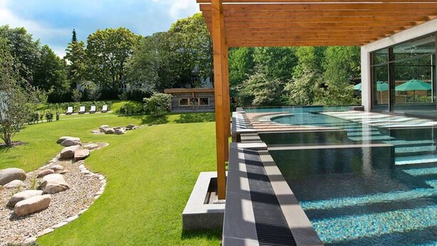 Un espace piscine extérieur moderne, agrémenté d’une pergola en bois, d’une pelouse bien entretenue et d’un chemin de pierre menant à la piscine.