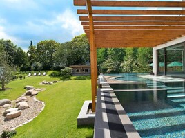 Ein moderner Poolbereich im Freien mit einer Holzpergola, einem gepflegten Rasen und einem Steinweg, der zum Pool führt.