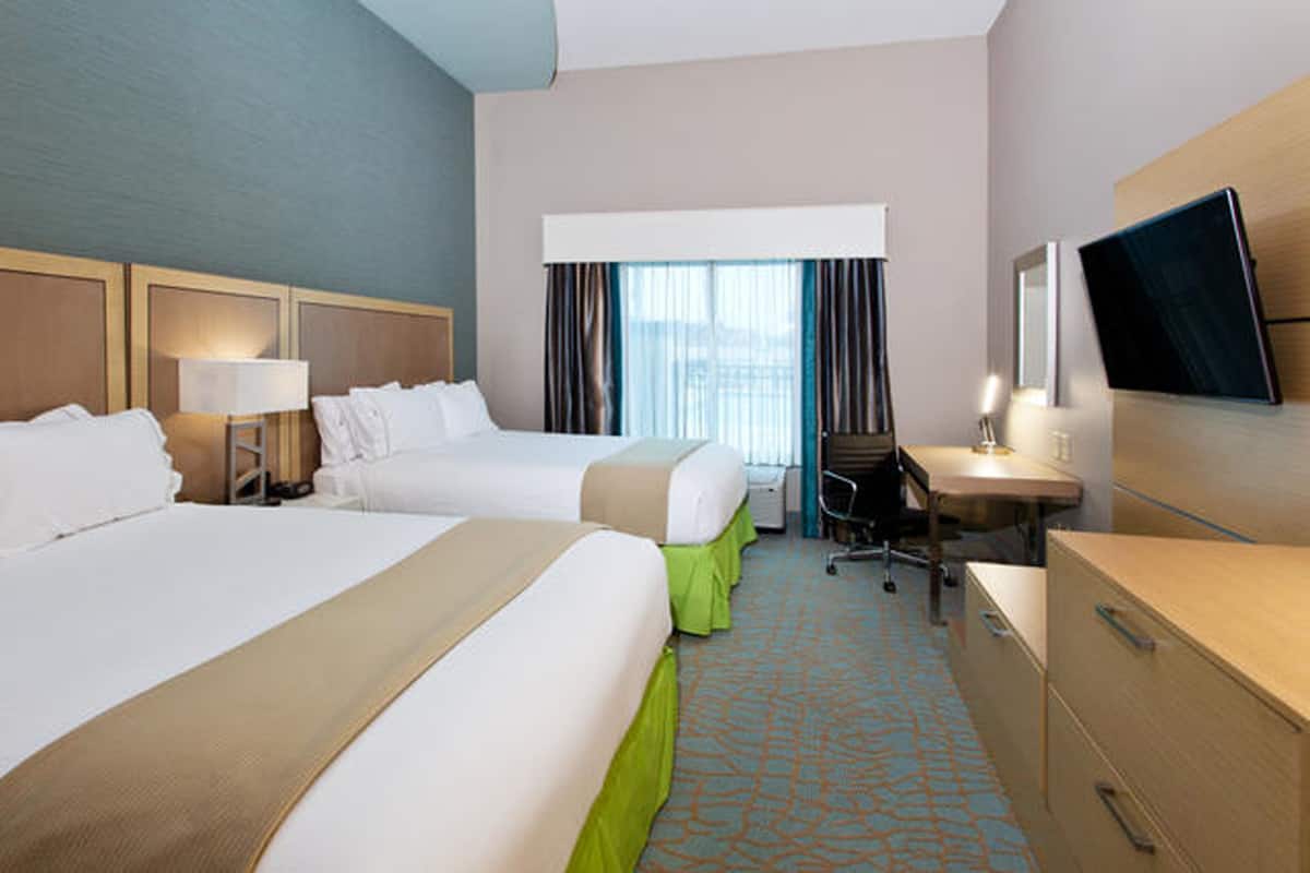 Une chambre d’hôtel avec deux lits, un bureau, une chaise, une télévision et une fenêtre avec des rideaux.