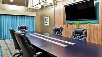 A conference room with a long table, four chairs, a large flat-screen TV, and a framed picture on the wall.