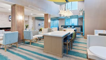 Eine moderne Hotellobby mit einer zentralen Insellounge, einer Sitzecke mit gemusterten Stühlen und einem großen Fenster mit Vorhängen.