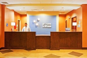 Zona de recepción de un hotel con pared azul que muestra el nombre y logotipo del hotel, dos mostradores de recepción de madera y un suelo de baldosas.