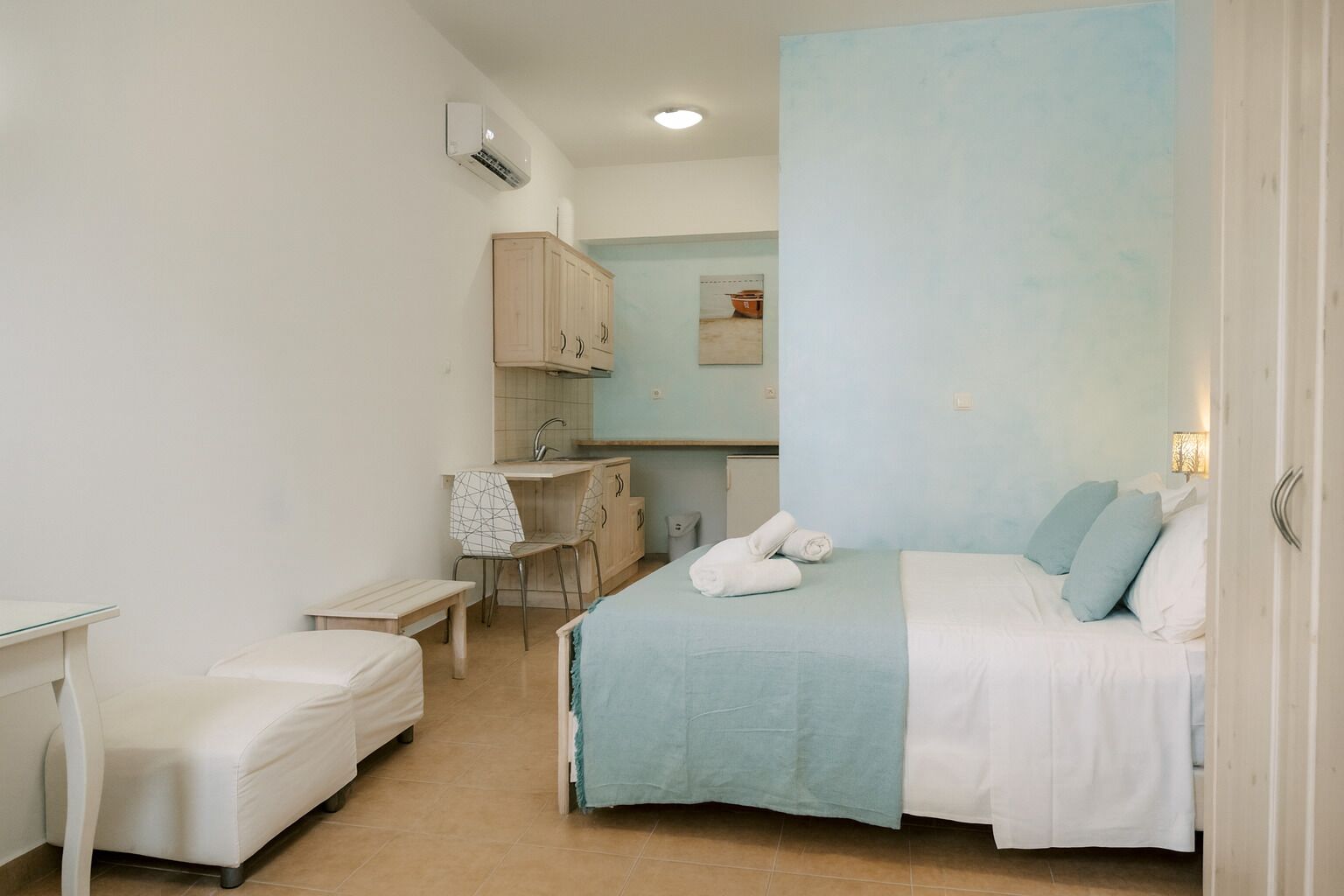Une chambre compacte comprenant un lit, un petit bureau et une kitchenette.
